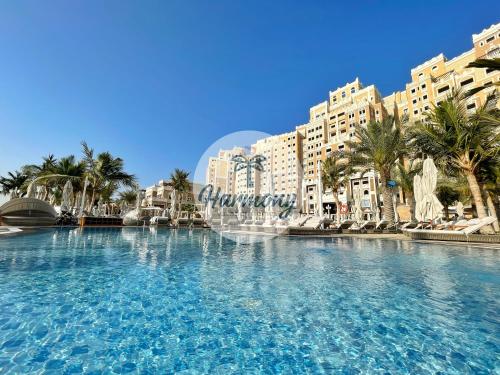 a large swimming pool with palm trees and buildings at Harmony Vacation Homes - BALQIS Residence in Dubai