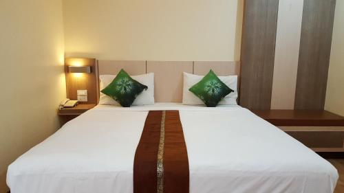 a bedroom with a large white bed with green pillows at Kaen Nakorn Hotel in Khon Kaen