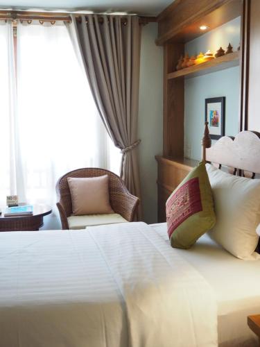 a bedroom with a white bed with a chair and a window at Rich Lanna House in Chiang Mai