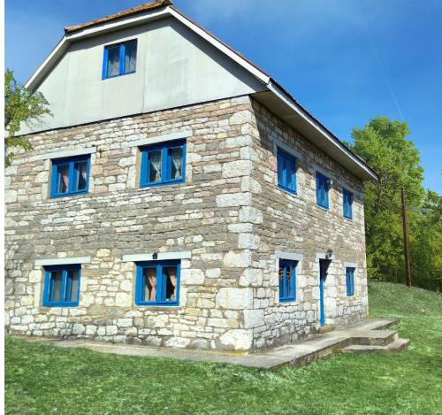 una casa de piedra con ventanas azules en una colina en Etno kuća Krvavac, en Pljevlja