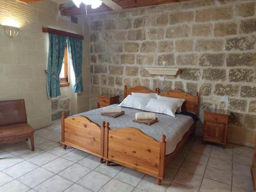 a bedroom with a wooden bed and a stone wall at MJ Farmhouse B&B in Xagħra