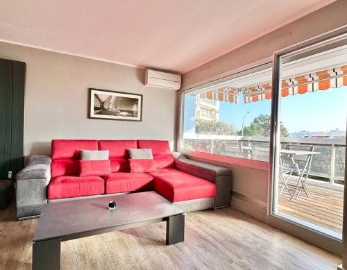 - un salon avec un canapé rouge et une grande fenêtre dans l'établissement Beautiful apartment - Air Conditionning -Pool -10min Beach -Parking near, à Antibes