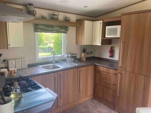 a kitchen with wooden cabinets and a sink and a window at 2 bedroom chalet in Chwilog on the Llyn Peninsula in Pwllheli