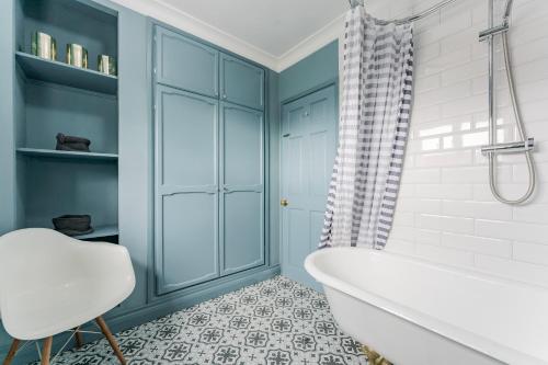 een blauwe badkamer met een bad en een stoel bij The Old Concert Hall - Norfolk Cottage Agency in Holt