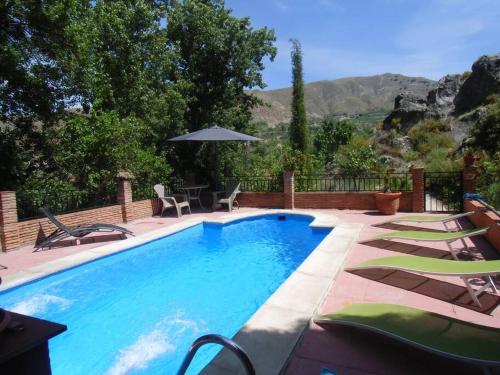 a swimming pool with chairs and an umbrella at Cortijo La Mata in Granada
