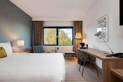 Cette chambre comprend un lit, un bureau et une fenêtre. dans l'établissement Hotel De Ruwenberg Den Bosch - Sint Michielsgestel, à Sint Michielsgestel