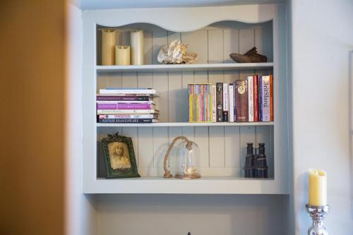 a book shelf filled with books and a candle at The Great William St. Cottage in Stratford-upon-Avon