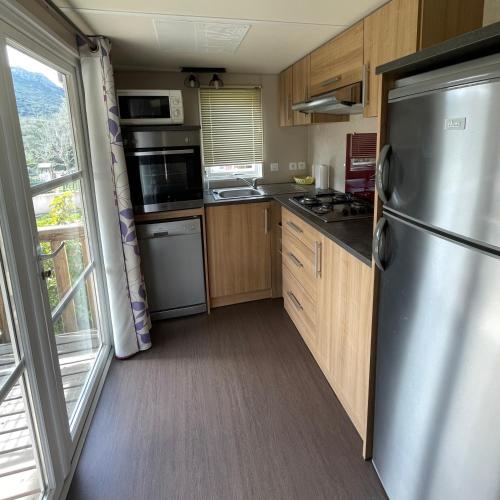 una cocina con nevera de acero inoxidable y armarios de madera en Parc Résidentiel La Listra - Bungalow, en Belgodère