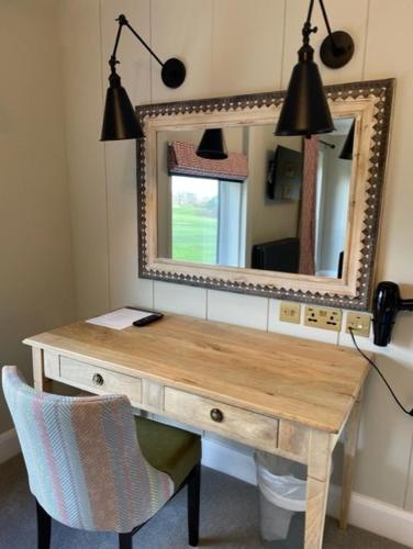 a wooden desk with a mirror and a chair at Cottesmore Hotel Golf & Country Club in Crawley