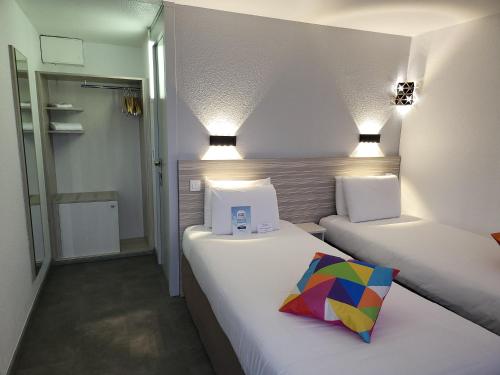 two beds in a small room with a colorful pillow at Kyriad Bellegarde - Genève in Bellegarde-sur-Valserine
