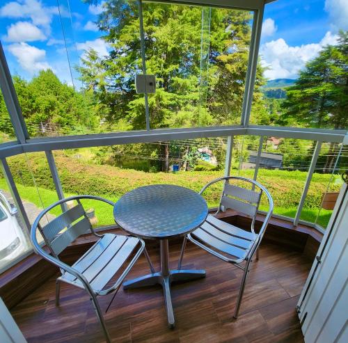 - une table et des chaises sur une terrasse couverte avec une fenêtre dans l'établissement Pousada Bliss House - Opções de suites com hidromassagem, à Campos do Jordão