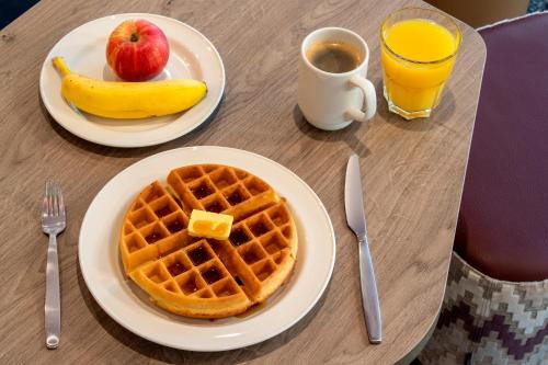 a table with two plates of waffles and an apple and orange juice at Hampton By Hilton London City in London