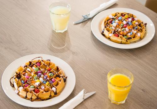 two plates of waffles on a table with two glasses of orange juice at Hampton By Hilton London City in London