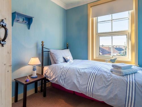 a blue bedroom with a bed and a window at Elf Cottage in Heacham