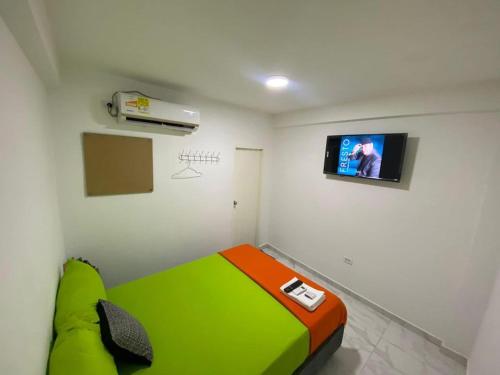 Habitación con cama verde y TV en la pared. en Hotel Aventura Riohacha en Riohacha
