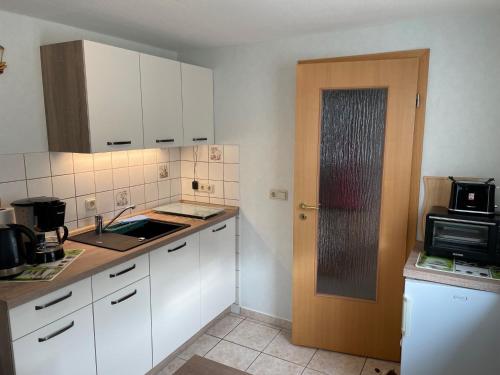 a kitchen with white cabinets and a sink and a door at Ferienhaus Waldglück in Tanne
