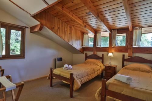 two beds in a room with wooden ceilings and windows at Bustillo 7500 in San Carlos de Bariloche