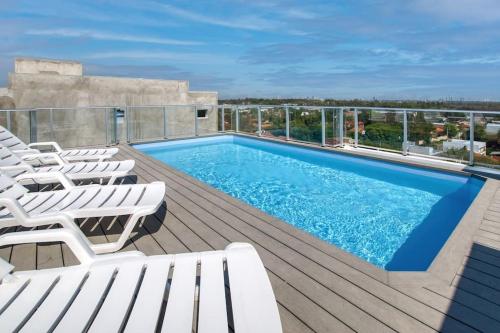 einen Pool auf einer Terrasse mit weißen Liegestühlen in der Unterkunft Elegante y fino departamento a estrenar! in La Mercedes