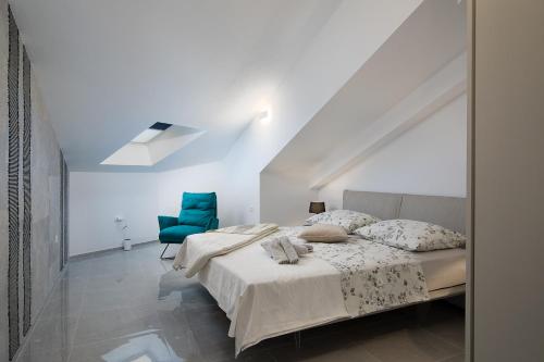 a white bedroom with a bed and a blue chair at Apartman Damjan in Pješčana Uvala
