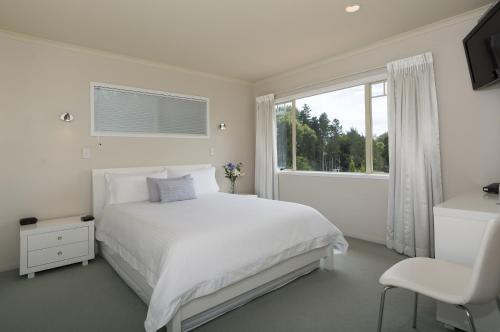 a white bedroom with a white bed and a window at Seascape Villa B&B in Tauranga