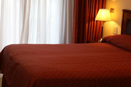 a bedroom with a bed with a red comforter and a window at Hotel Amsterdam in Mar del Plata