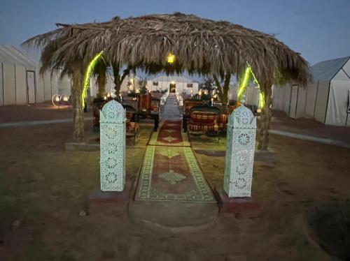 a restaurant with a straw umbrella and tables and chairs at Merzouga Top Luxury Camp in Merzouga