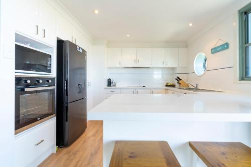 a kitchen with white cabinets and a black refrigerator at Sails Apartments in Forster