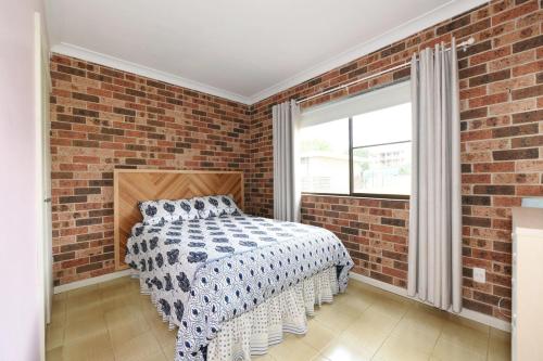 Dormitorio con paredes de ladrillo, cama y ventana en Excellent Location - Belle Escapes Jervis Bay, en Vincentia