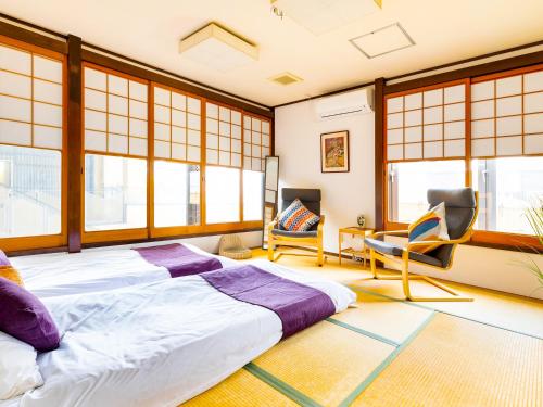 a bedroom with a large bed and chairs and windows at Nara Guesthouse 3F in Nara