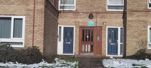 un bâtiment en briques avec des portes bleues et de la neige au sol dans l'établissement Lovely 3 Bed Apartment Near QE Hospital Harborne Birmingham New, à Birmingham