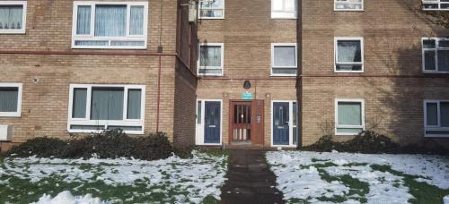 um edifício de tijolos com uma porta vermelha na neve em Lovely 3 Bed Apartment Near QE Hospital Harborne Birmingham New em Birmingham