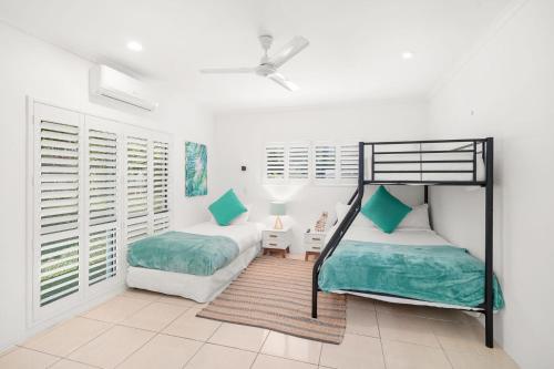 2 camas en una habitación con paredes y ventanas blancas en Belle Escapes Under the Mango Tree Holiday Home en Trinity Beach