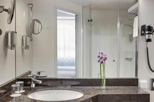 een badkamer met een wastafel, een spiegel en paarse bloemen bij IntercityHotel Ulm in Ulm