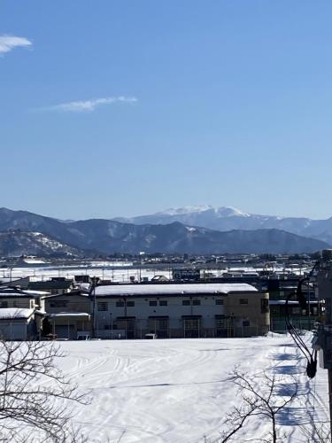a snow covered parking lot with a building in the background at Yamagata Guesthouse山形ゲストハウス in Murayama