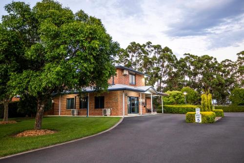 a brick house with a tree and a driveway at Hawkesbury Race Club Motel in Windsor