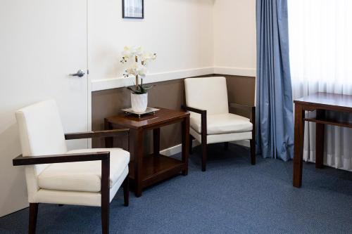 a room with two chairs and a table with a vase of flowers at Hawkesbury Race Club Motel in Windsor