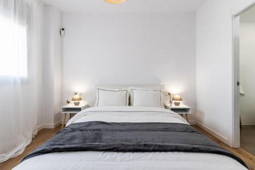 a white bedroom with a large bed with two tables at Acojedor y exclusivo loft by Lofties in Terrassa