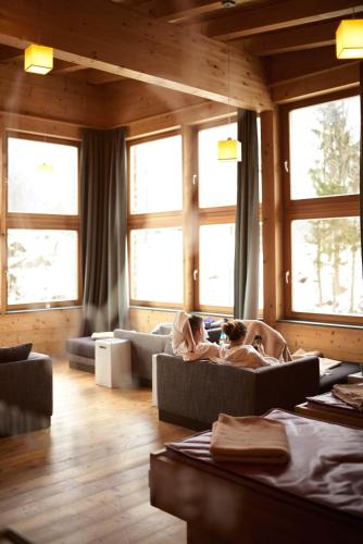 a woman laying on couches in a room with windows at Holzhotel Forsthofalm in Leogang