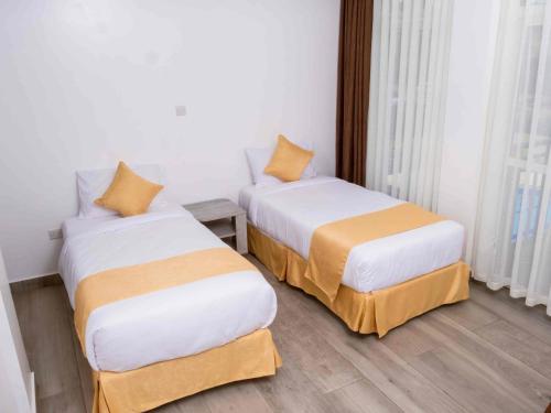 2 camas en una habitación de hotel con sábanas blancas y naranjas en KISIMANI ECO RESORT & SPA LTD en Isiolo