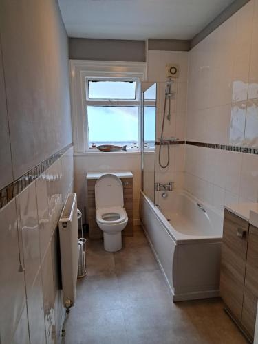 a bathroom with a toilet and a tub and a window at Llandudno apartment, quirky pub with tropical beer garden in Llandudno