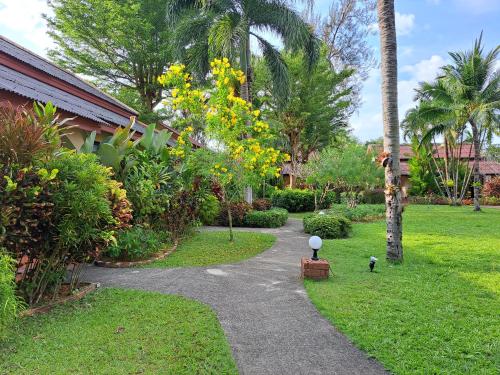 a walkway through a garden with yellow flowers and palm trees at Jasmin Resort - SHA Plus in Khao Lak