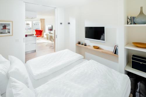 um quarto branco com mobiliário branco e uma televisão em Neys Beach Loft em Norderney