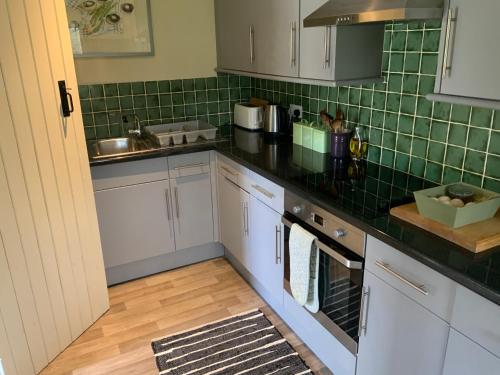 una cocina con armarios blancos y azulejos verdes en la pared en Gardeners Cottage, en Crudwell