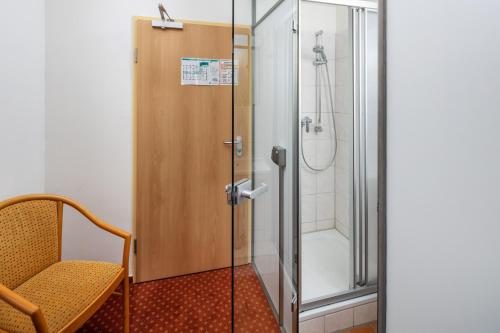 a shower with a glass door next to a chair at Academy Lodge Boardinghouse in Hamburg