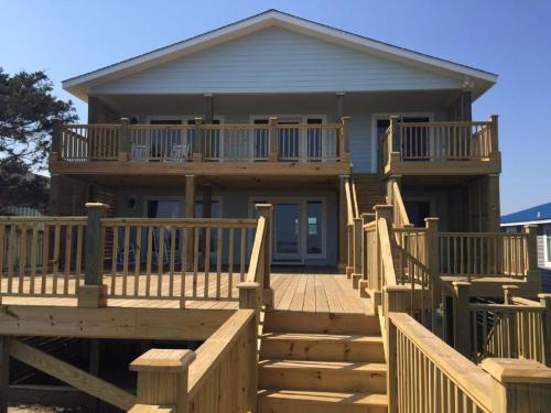 a house with a large deck with stairs leading to it at Dune Deck South - Duplex in Holden Beach