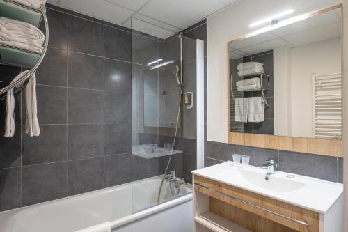 ein Badezimmer mit einem Waschbecken, einer Badewanne und einem Spiegel in der Unterkunft Apparthotel Privilodges Le Royal in Annecy