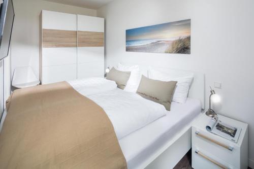 een witte slaapkamer met een bed en een schilderij aan de muur bij Sommerdeich4you in Norderney