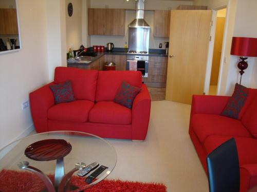 カーディフにあるRiverbank Penthouse and Apartmentsのリビングルーム(赤いソファ2台、ガラステーブル付)