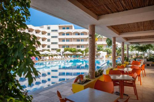 een resort met een zwembad en tafels en stoelen bij IALYSSOS BAY HOTEL in Ialyssos