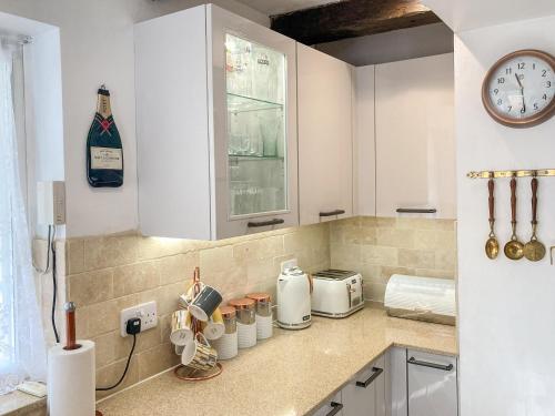 a kitchen with white cabinets and a clock on the wall at Borough Beck Cottage in Helmsley